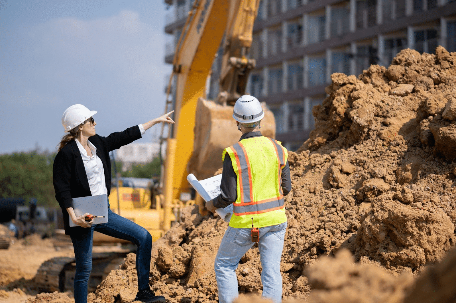 A construction company manager directs her employee next to a pile of dirt.