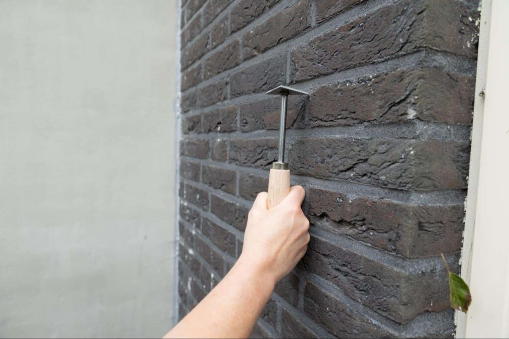 A contractor tests the structural solidity of a masonry wall with a masonry jointer.