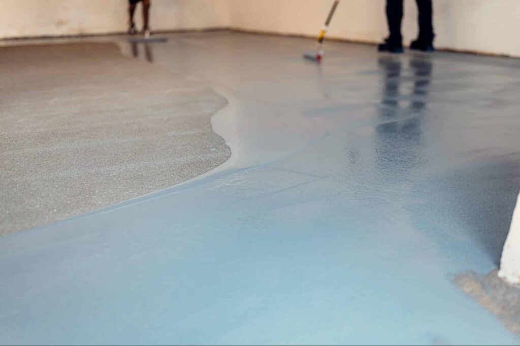 Two workers apply epoxy resin coating to a commercial space flooring.