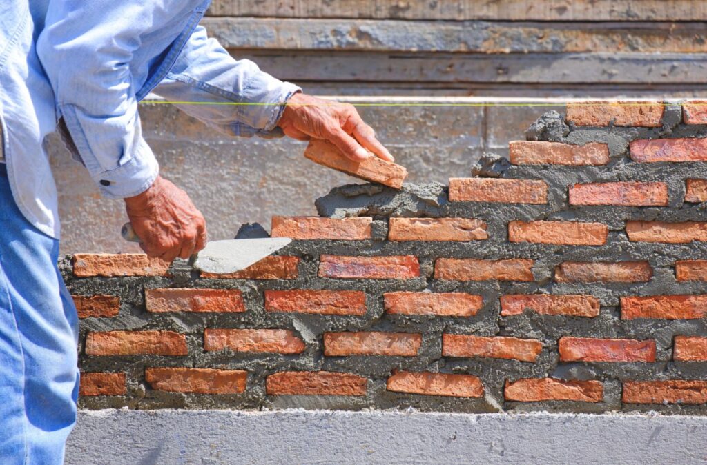 Close-up of a mason laying bricks to construct a low fence wall for a home.