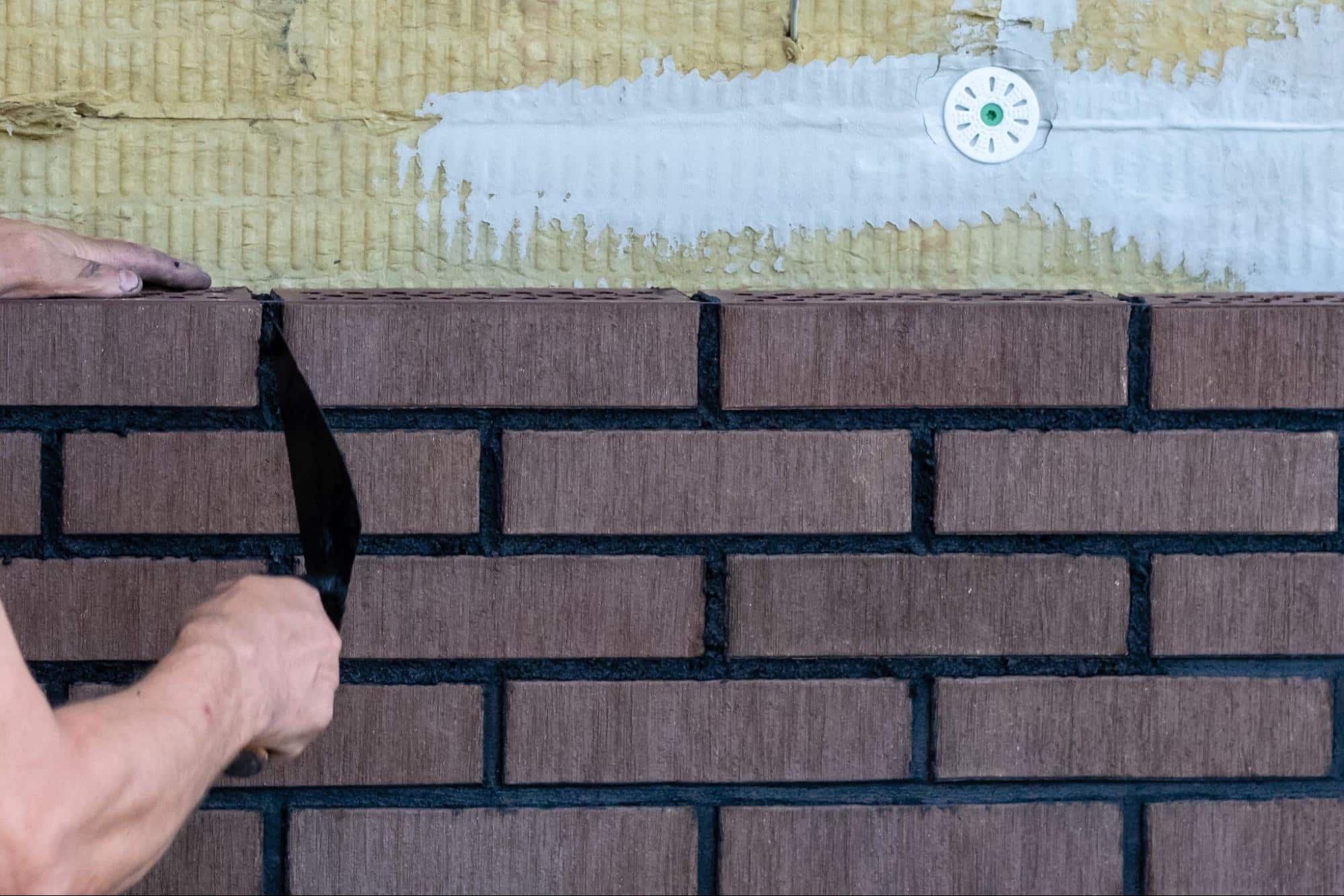 A close-up of a mason tuck-pointing a brick wall with precision hand tools